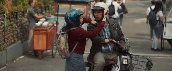 A girl adjusts a man's helmet on a motorcycle in "Panggil Aku Ayah".
